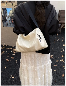 Detail of beige quilted crossbody bag featuring textured fabric and wide black strap