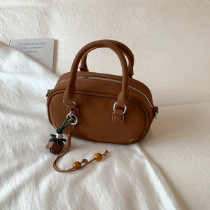 Close-up of brown suede Boston bag with silver hardware and decorative floral charm