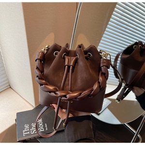 Close-up of brown leather bucket bag with braided handle and drawstring closure