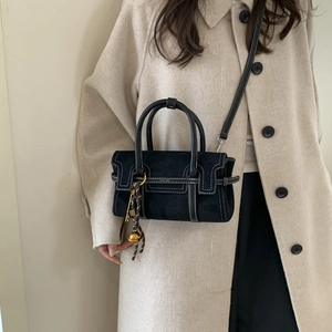 Detail of a black suede square crossbody bag with white stitching and golden charms