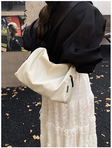 Detail of cream plaid crossbody bag with wide black textile strap and zipper closure