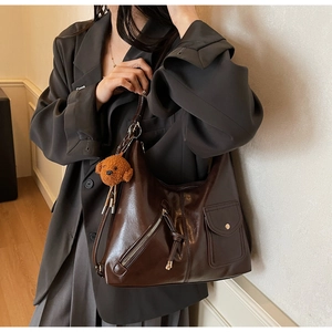 Detail of dark brown leather punk style shoulder bag with pockets and plush puppy charm