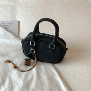 Detail of black crossbody bag featuring floral pendant and silver zipper on white fabric