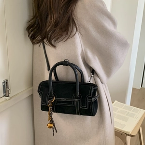 Detail of black suede handbag with contrast stitching and golden bell charm accessory