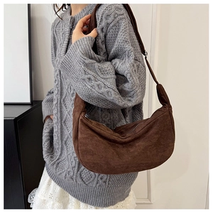 Detail van donkerbruine suède hobo tas gestyled met een grijze gebreide trui