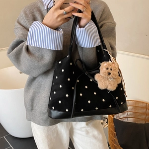 Dettaglio della borsa tote nera a pois con manico in pelle e ciondolo a forma di orso