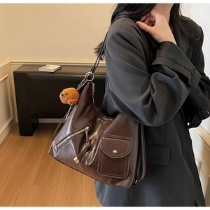 Detail of dark brown glossy hobo bag featuring metal zippers and a plush bear charm