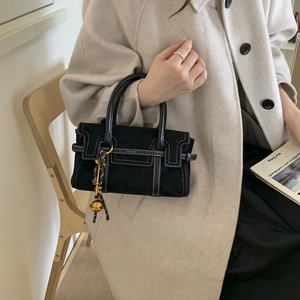 Close-up of black suede handbag with contrast stitching and golden bell charm detail