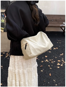 Detail of cream plaid shoulder bag with black zipper and soft texture in outdoor setting