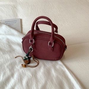 Detailed view of burgundy oval handbag with silver zipper and floral charm on white fabric