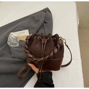Detail of dark brown patchwork bucket bag with braided handle and drawstring on bedsheets