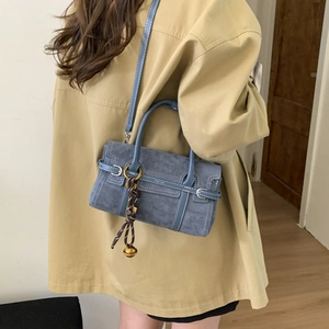 Detail view of dusty blue suede crossbody bag with decorative woven pendant and bell