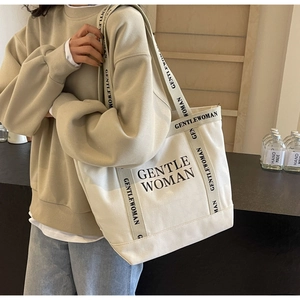 Dettaglio della grande borsa tote in tela bianca con scritta GENTLEWOMAN e manici neri