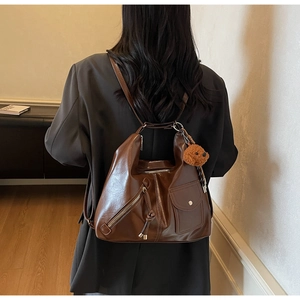 Detail of vintage brown leather convertible bag worn with black blazer and bear charm