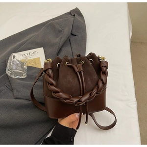 Detail of a deep brown bucket bag with suede texture, woven handle and drawstring closure