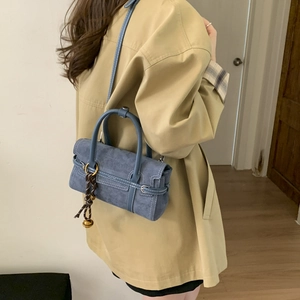 Blue suede crossbody bag with white contrast stitching and woven charm detail