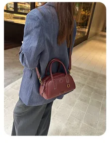 Dettaglio della borsa bowling in pelle bordeaux con cuciture bianche e tracolla regolabile