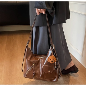 Close-up of brown leather shoulder bag with zipper details and a teddy bear charm