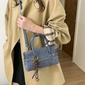Detail of blue crossbody bag featuring white contrast stitching and vintage key charm
