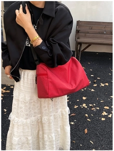 Close-up of red plaid pillow crossbody bag featuring black strap and zipper details