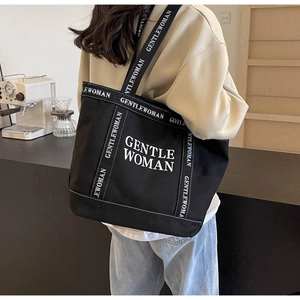 Dettaglio della borsa tote in tela nera con scritte Gentlewoman bianche sulla tracolla