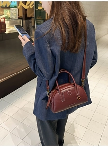 Deep burgundy pebbled leather bowling bag detail with gold hardware on a blue blazer