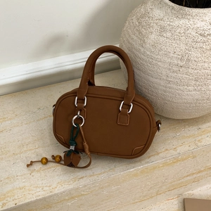 Close-up of brown Boston handbag with walnut charm detail on stone surface