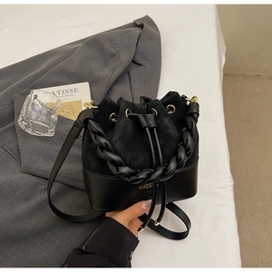 Close-up of black drawstring bucket bag featuring braided handle and textured leather stitching