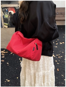 Detailed view of large red plaid crossbody bag with wide black strap on female model