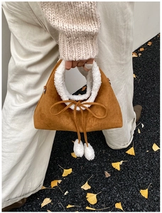 Détail du sac en daim marron avec bordure en laine blanche et pompons décoratifs