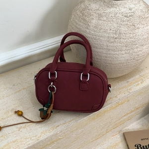 Macro detail of bordeaux bosto bag with decorative leaf charm on marble steps
