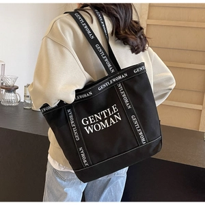 Dettaglio della borsa tote in tela nera con testo GENTLEWOMAN bianco sulla tracolla larga