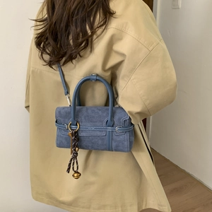 Detail of blue suede crossbody bag showing woven pendant and white stitching texture