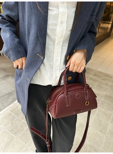 Detail of burgundy pebbled leather bowling bag with contrast stitching and gold hardware