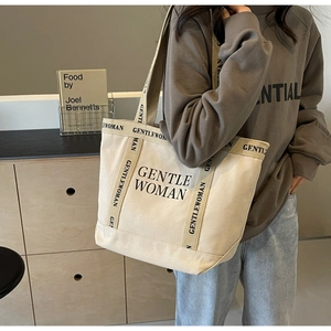 Dettaglio della borsa tote in tela color crema con logo GENTLEWOMAN e tracolla