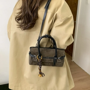 Detail of suede crossbody bag with contrast stitching and golden bell charm accessory