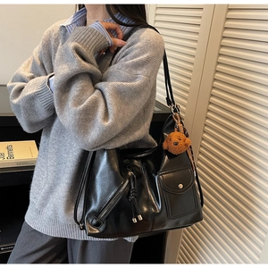 Close-up of a black punk-style shoulder bag with a teddy bear charm on a model