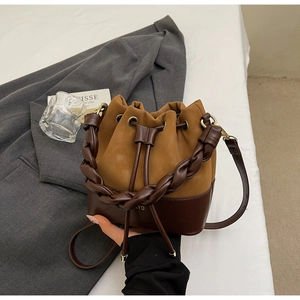 Detail of two-tone bucket bag featuring woven handle and adjustable shoulder strap
