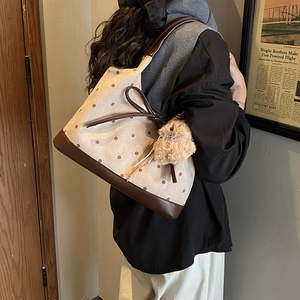 Dettaglio della borsa tote beige a pois con fiocco in pelle marrone e ciondolo a coniglio