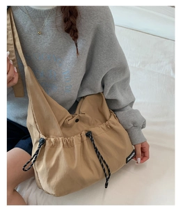 Detail view of khaki drawstring crossbody bag with fashion label and adjustable strap