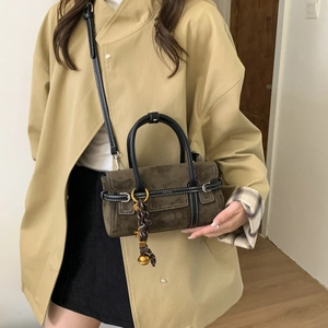 Close-up of a dark brown suede mini bag featuring contrast stitching and a metal pendant