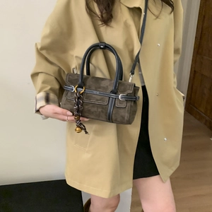 Detailed shot of brown suede bag with black leather piping and gold bell scarf charm