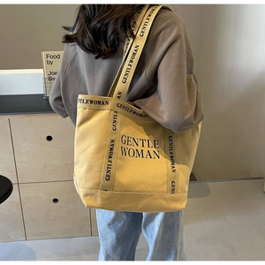 Dettaglio della borsa tote in tela gialla con logo nero e ampi spallacci per spalla