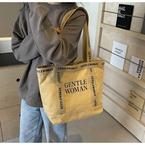 Dettaglio di una borsa tote in tela beige con scritta GENTLEWOMAN portata a spalla