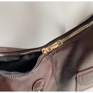 Detail of golden zipper closure and polished leather texture on dark brown shoulder bag