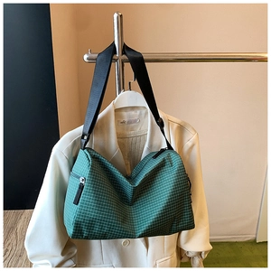 Detail view of a green plaid tote bag with black strap against a white blazer