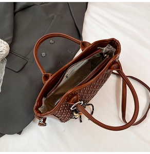 Detail view of deep brown woven texture handbag with double handles and zipper closure