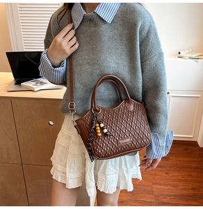 Detail of brown woven bucket bag featuring wooden bead charm and crossbody strap
