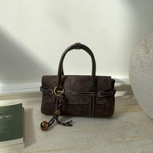 Detail of dark brown suede handbag with contrast stitching and decorative bell pendant