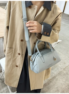 Detail of light blue lychee pattern leather bowling bag worn with a beige trench coat